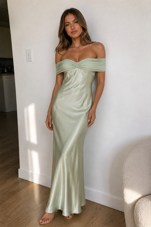 Woman wearing a light green off-shoulder gown standing against a white wall.